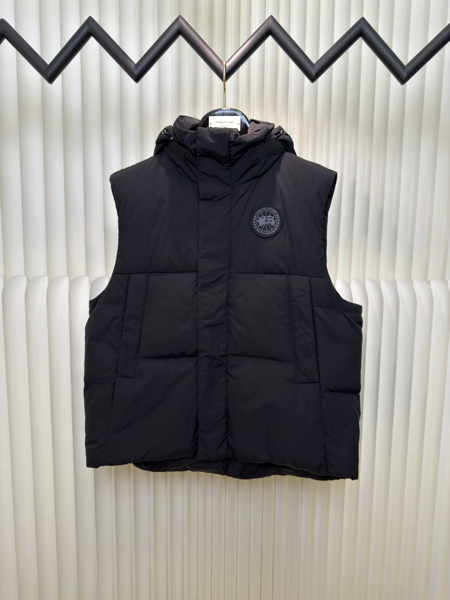 P760 Big Goose Logo Hooded Down Vest is made of high-quality protective nylon fabric, which not only enhances the wear resistance of the surface, but also takes into account wind resistance, ensuring excellent performance in various harsh weather conditions.  90 national standard high-quality white duck down: selected high-loft down, weighing 170g, light and warm, with excellent temperature locking performance and good resilience.  Three-dimensional quilting process: Precision thread reinforcement to prevent velvet drilling and ensure that the fluffy and resilient elasticity lasts as new.  Details: The ribbon is woven with polyester as the base. The brand letters are decorated on the ribbon through high-precision computer embroidery. The edges of the pattern are clear, the stitches are fine and even, and multiple layers of embroidery thread are stacked to enhance the three-dimensional effect. Size S M L XL
